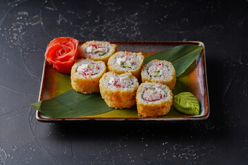 Tempura roll California on a plate. On black background with wasabi, ginger, bamboo leaf.