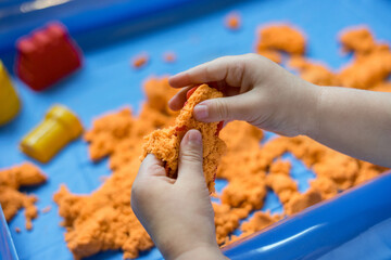 Close view of child's hands playing with kinetic sand. Children's creative game for early development and fine motor skills. - obrazy, fototapety, plakaty