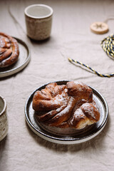 Cinnamon swirl brioche or Cinnamon roll bun and cups of cocoa on greige linen tablecloth. Homemade baked swedish cinnamon roll. Kanelbullar. Cozy winter breakfast