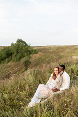 Fototapeta na wymiar An african american man and his pregnant wife sits in embrace on the hill and enjoying sunset
