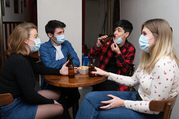 Four friends wearing face masks in a pub. One of them is drinking and other are wearing their masks. New normal in bars.