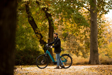 Young man with electric bicycle in te autumn park