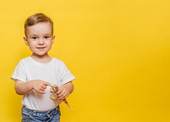 Cute laughing little boy on a yellow background with a dinosaur toy in his hands. Copy space.