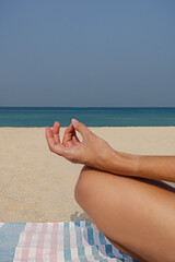Blonde young girl practices yoga and meditation in the lotus position on the beach on a sunny day.
