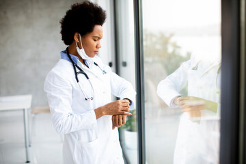 Black female doctor standing by the office window and checking time on watch