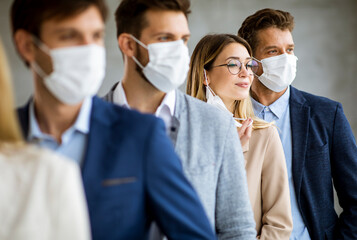 Business woman taking off her protective facial mask and looking at the camera with her team members standing in the line