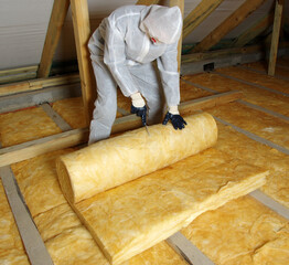 Worker thermally insulating house attic with glass wool