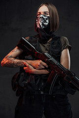 Fototapeta premium Armed with ak74 rifle and weared with mask stylish female mercenary poses in dark background.