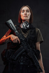 Fototapeta na wymiar Stylish and martial woman with short haircut and tattooed arm poses holding ak74 rifle in dark background.