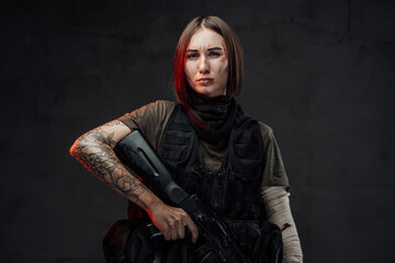 Dreseed in dark armour military woman with short haircut holds rifle with tattooed and bandaged...
