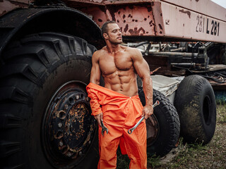 Posing near abandoned vehicle athlete in orange uniform with naked torso holding instruments in the open air.