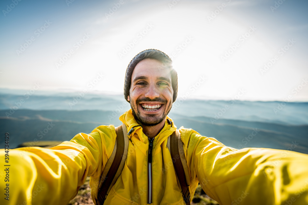 Wall mural happy hiker taking a selfie on the top of a mountain - smiling man smiling looking camera - handsome