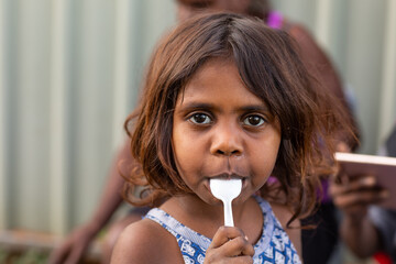 little kid with plastic spoon in mouth looking at camera