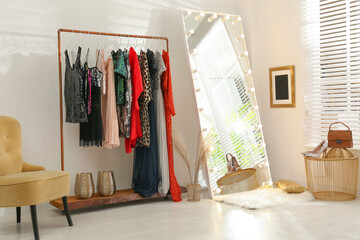 Rack with different stylish women's clothes and mirror indoors