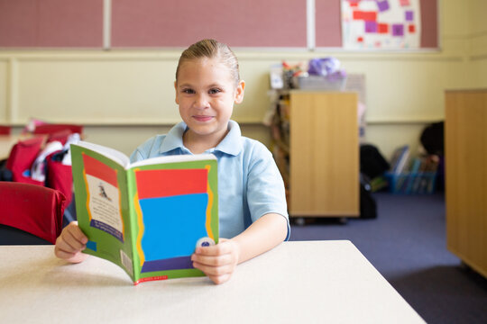 Indigenous girl primary school student with a book in a classroom