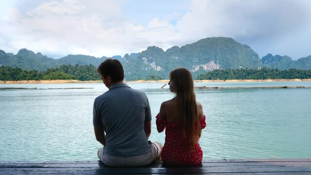 Back View of Couple in Love Sitting Together on Date, Man Flirting, Touching Woman Booty and Getting Funny Slap, Fun and Laughing Together. Pair of Travel People at Lake with Mountains