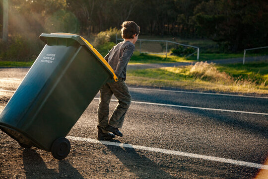 Young boy doing job taking bin across the road