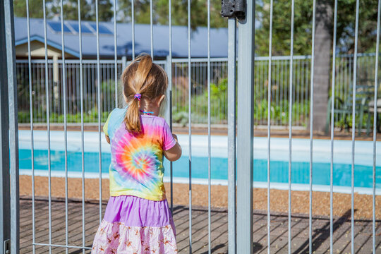 Little girl standing safely outside pool fence gate looking in