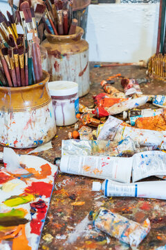 An messy artist's table covered in colourful paint and brushes