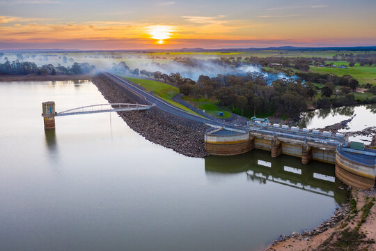 Aerial view of a water tower in a reservoir at sunset with smoke drifting across.