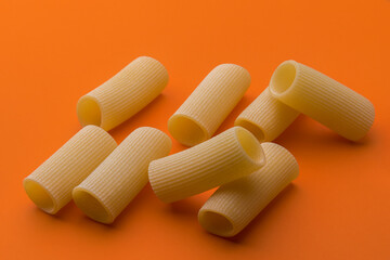 Paccheri macaroni Italian dry raw pasta bronze drawn, rough paste from Gragnano,Naples,Italy, close up on orange background