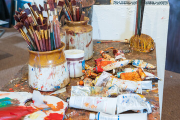 An messy artist's table covered in colourful paint and brushes
