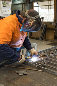 A tradesman wearing high vis clothing welding steel on a workbench