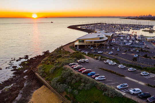 Aerial view of a bay side yacht club and car park above a beach at sunset