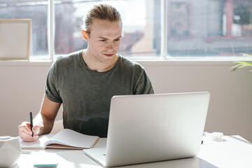 Male designer looking at a laptop screen in a bright white studio