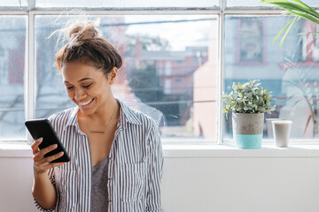 Young creative female smiling and reading her phone at a studio window
