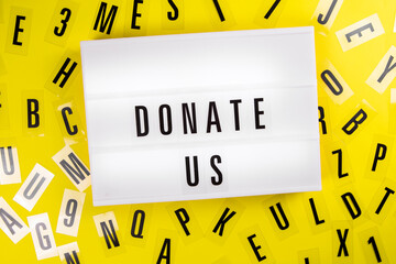 Donate Us message on lightbox on scattered letters background of plastic alphabet. charitable foundation, call for donations, compassion, money transfers to charity organizations, philanthropy concept