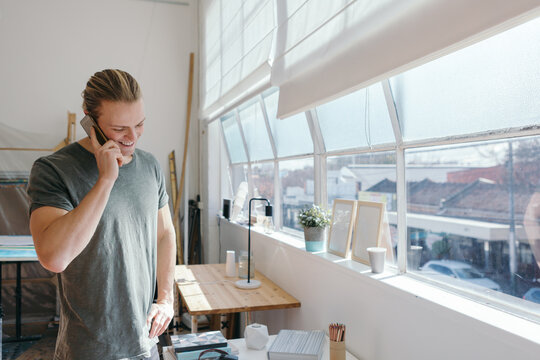 Casual guy on the phone smiling in a bright studio work space