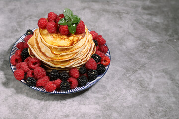 Plate of pancakes with raspberries and blackberries on a gray background .Russian cuisine. Copy space
