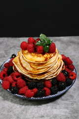 Russian cuisine dish-homemade pancakes with raspberries and blackberries on a gray background.Copy space