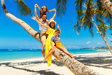 Young happy family-mom, dad, daughter and son having fun on a coconut tree on a sandy tropical...