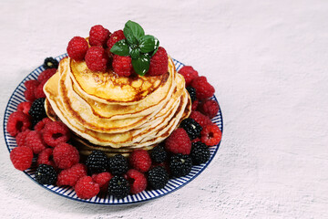 Delicious dish of Russian cuisine-homemade pancakes with raspberries and blackberries on a light background.Copy space