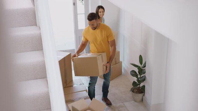 Couple Walk Through Front Door Of New Home Carrying Boxes On Moving Day Before Hugging And Kissing As They Look Around - Shot In Slow Motion