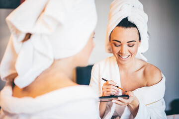 Obraz na płótnie Canvas Young women wearing bathrobe sitting at hotel room, and applying makeup.