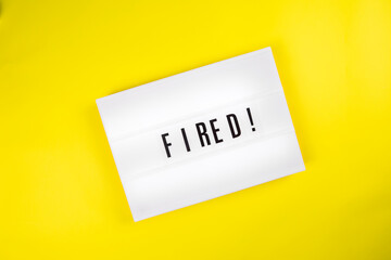 Fired! message on lightbox on yellow background isolated. Top view, flat lay. Economic crisis, downsizing, staff cuts, mass dismissals, job search, labor exchange, uncertainty about future concept