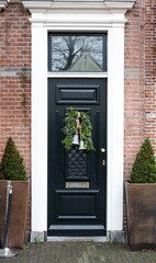 House facade with vintage front door decorated with christmas wreath with bells. Black vintage door with festive christmas decor. Porch European style in brick house
