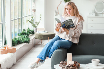 Beautiful young woman in warm sweater reading magazine at home