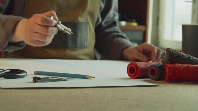 Close-up tailor makes markings on a sheet of paper with a pencil and compasses for making patterns for sewing products made of genuine leather. Slow motion