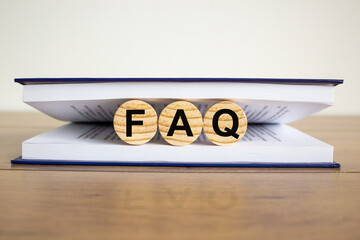 Concept word 'FAQ, frequently asked questions' on wooden circles between pages of a book on a...