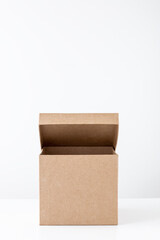 Half-open cardboard box on a white table on the back of a white wall. Place for text. The concept of a minimalist, ecological gift.