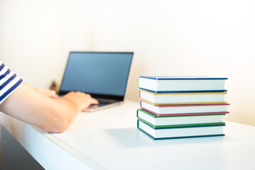 Person typing on Laptop with books stacked on its side. Searching in the Internet.