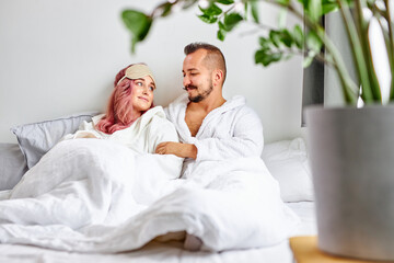 Fototapeta premium couple enjoy rest in bed together, relax time. caucasian married couple in bathrobes are in love, in light bedroom