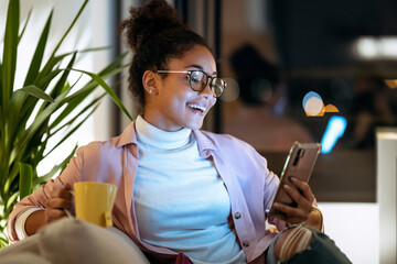 Happiness young entrepreneur woman using her smart phone while drinking a cup of coffee sitting on couch in the office. - Powered by Adobe