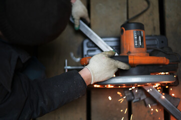 Photo of a welder's hand working cuts metal with a saw in a workshop