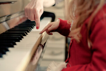 A piano lesson, with a female teacher pointing at a key to her kid student with a finger.
