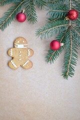 Christmas composition. Gingerbread man in a medical mask on a wooden background with red balls and a green Christmas tree.